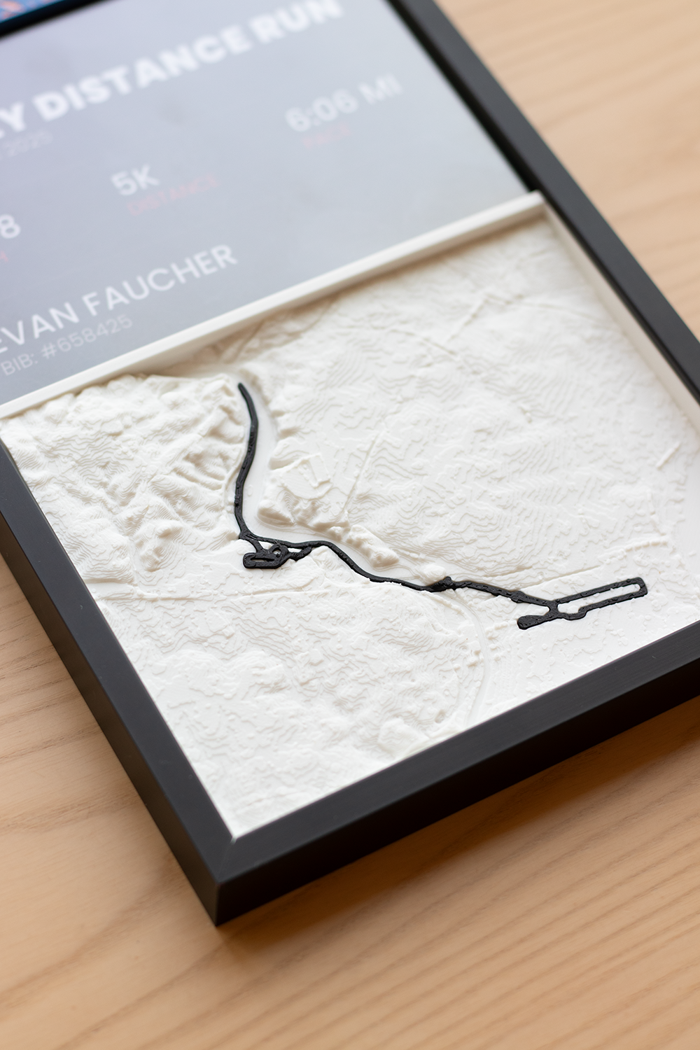 3D printed terrain map of a race course in a black frame, with the route raised in black